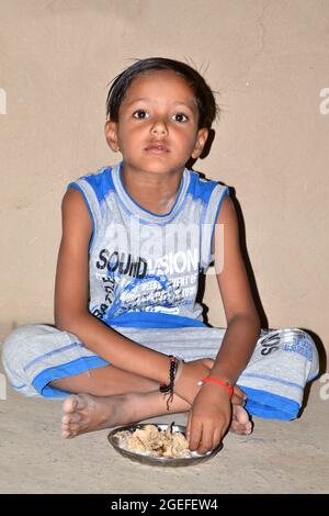 Enfant rural indien mignon portant un short et un t-shirt mangeant du pain avec du lait. Banque D'Images