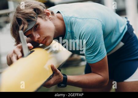 Sportsman Single Scroll man rameur sportif vérifier son bateau. Un sportif caucasien vérifie son canot. Beau blond jeune homme porter des vêtements de sport et montre de poignet. Préparation à la compétition sportive Banque D'Images