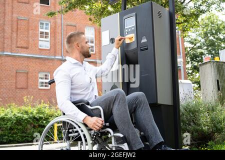 Homme handicapé en fauteuil roulant payant un ticket de parking utilisant la machine Banque D'Images