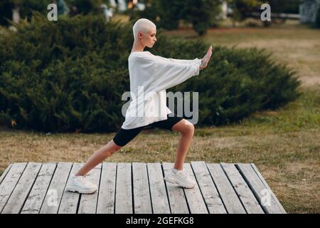 Portrait d'une jeune femme européenne à poil court souriant faisant du wushu Qigong dans le parc d'été. Belle fillette blonde heureuse en plein air. Banque D'Images