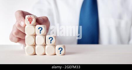 Homme d'affaires place un cube avec symbole d'ampoule sur des cubes en bois à plusieurs niveaux avec des symboles de point d'interrogation. La créativité ou pour atteindre une solution en bussin Banque D'Images