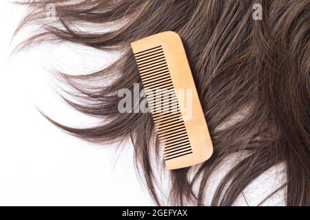 Cheveux bruns droits avec peigne en bois isolé sur fond blanc vue du dessus. Concept de soins capillaires Banque D'Images