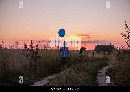 Happy Boy laisse aller des ballons au ciel. Courez le long du champ jaune. Belle carte d'été, anniversaire et liberté. Banque D'Images