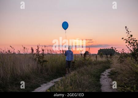 Happy Boy laisse aller des ballons au ciel. Courez le long du champ jaune. Belle carte d'été, anniversaire et liberté. Banque D'Images