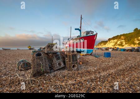 Potes de homard et bateau de pêche rouge sur la plage de galets au lever du soleil, bière, côte jurassique, Devon, Angleterre, Royaume-Uni, Europe Banque D'Images