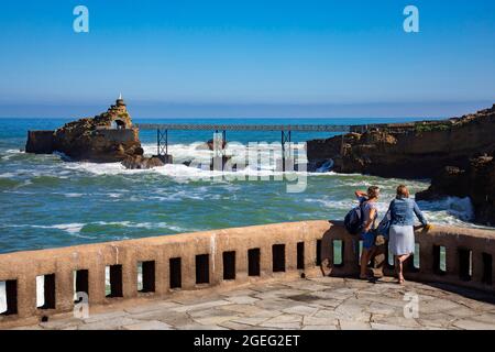 Biarritz (sud-ouest de la France) : vue arrière de deux femmes face à la mer et au Rocher de la Vierge Marie avec sa passerelle le long de la côte basque Banque D'Images