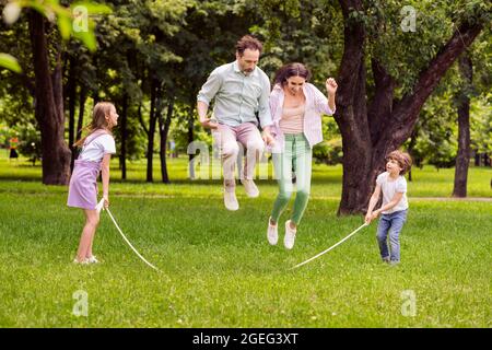 Photo de charmant funky famille habillée tenue décontractée jouant corde jumping souriant à l'extérieur de la rue de ville urbaine Banque D'Images