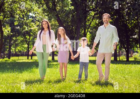 Portrait de attrayant adopté favoriser gai famille papa maman passer du temps sur l'herbe verte marchant l'air frais à l'extérieur Banque D'Images