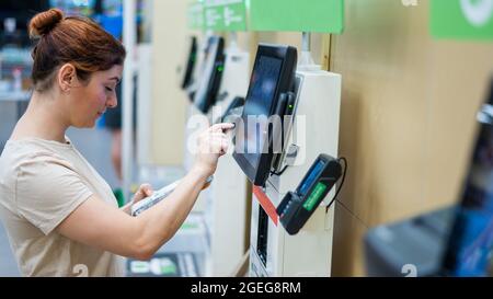 Une femme frustrée utilise un comptoir de caisse libre-service. La fille ne comprend pas comment acheter indépendamment des provisions dans le supermarché sans un vendeur Banque D'Images