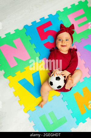 Petite fille sur le tapis avec des lettres et ballon de football Banque D'Images