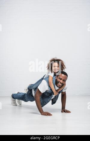 joyeux afro-américain fille piggysoutenant heureux papa faire des push up sur gris Banque D'Images