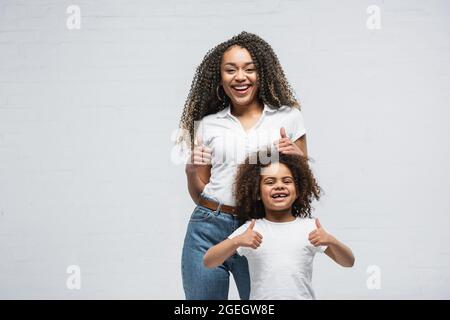 une jeune fille afro-américaine excitée avec une maman qui montre les pouces sur le gris Banque D'Images