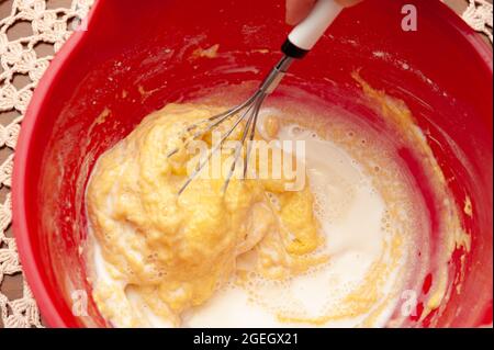 Mélanger le jaune d'œuf avec la farine de blé et le lait dans un bol en plastique rouge. Fond de nappe en crochet. Vue de dessus. Gros plan. Banque D'Images