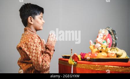 Studio photo d'enfant pendant le festival ganesha avec robe traditionnelle priant devant l'idole ganapati sur fond gris. Banque D'Images