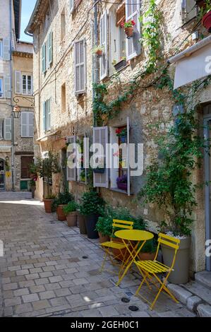 Vence (sud-est de la France) : table, chaises et fleurs le long de la façade d'une maison dans la rue "rue de l'Eveche" au coeur du Vieux T médiéval Banque D'Images