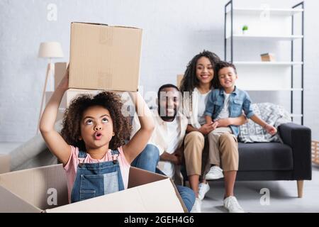 enfant afro-américain excité tenant une boîte en carton près de la famille floue Banque D'Images