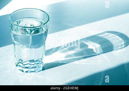 Un verre avec de l'eau claire et claire et des ombres vives se tient sur une table blanche Banque D'Images