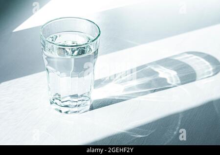 Un verre avec de l'eau claire et claire et des ombres vives se tient sur une table blanche Banque D'Images