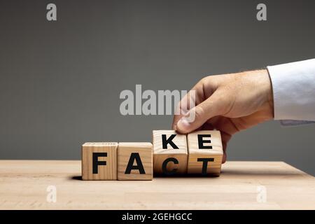 La main masculine fait basculer des cubes en bois avec des mots faux à fait sur une table en bois sur fond gris. CopySpace pour publicité. Banque D'Images