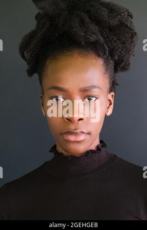 Jeune femme africaine en chandail noir debout sur fond noir. Banque D'Images