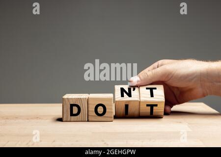 La main masculine fait basculer des cubes en bois avec des mots NE PAS faire sur la table sur fond gris. CopySpace pour publicité. Banque D'Images