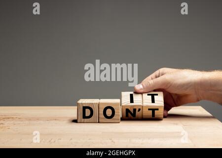La main masculine fait basculer des cubes en bois avec des mots NE PAS faire sur la table sur fond gris. CopySpace pour publicité. Banque D'Images