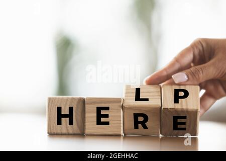 La main féminine fait des cubes en bois avec le mot ici pour aider sur la table en bois. CopySpace pour le design, la publicité, l'offre. Banque D'Images
