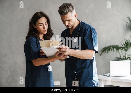 Deux médecins en uniformes médicaux discutant ensemble de l'anamnèse du patient, en tenant compte des résultats des tests à l'intérieur Banque D'Images