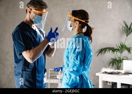 Deux médecins portant un uniforme médical de protection debout dans le cabinet, discutant Banque D'Images