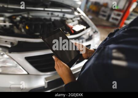 Gros plan des mains de mécanicien de voitures de course mixte portant une combinaison, à l'aide d'une tablette Banque D'Images