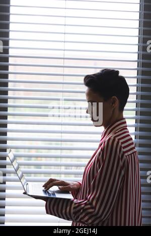 Une femme d'affaires caucasienne attentionnée se tenant debout à la fenêtre, en utilisant un ordinateur portable Banque D'Images