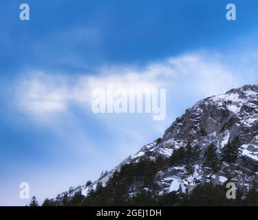 Des nuages qui soufflent sur une ridgeline du mont Monadnock mènent au sommet en hiver avec de la neige. Les conifères bordent la crête parmi les gros rochers. Banque D'Images