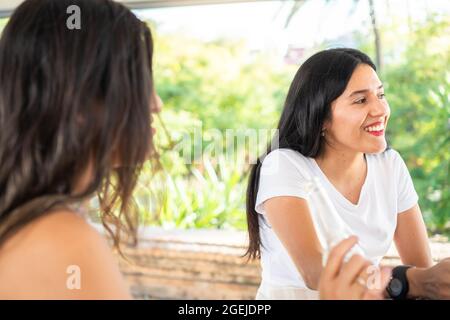 Jeune latina appréciant une soirée avec ses amis autour d'un verre. Femme ayant une belle conversation en bonne compagnie un jour ensoleillé. Fille hispanique souriante Banque D'Images