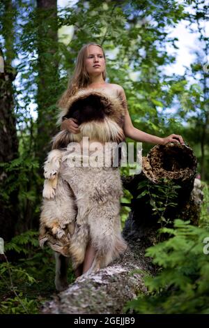 Fille sauvage vêtue de peaux d'animaux parmi les arbres de la forêt. Mise au point peu profonde. Banque D'Images