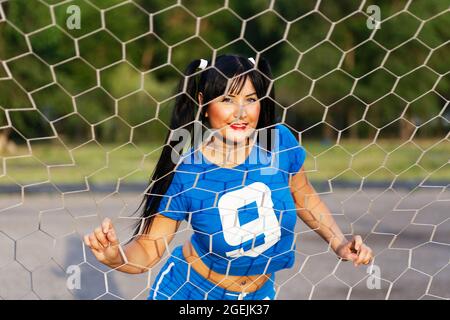 Une fille brune dans un uniforme de sport se tient derrière une porte de football et gardé derrière le filet de la porte Banque D'Images