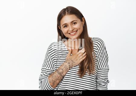 Merci. Une jeune femme en lambeaux se baissent de la main sur la poitrine, se présente, souriant et recevant des louanges ou des compliments, fond blanc Banque D'Images