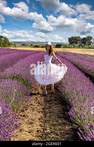 Bonne jeune femme jouant avec sa robe blanche au milieu d'un champ de lavande en fleur. Concept de bien-être et de bonheur. Banque D'Images