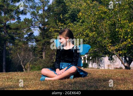 Une petite fille est assise seule à l'extérieur. Elle rêve de ce qu'elle voudrait être un papillon volant librement dans le ciel. Elle a sur un bleu et noir mais Banque D'Images