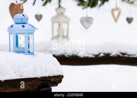 Lanterne bleue sur la neige et les coeurs accrochés à la guirlande de sapin dans le jardin. Décoration extérieure de Noël. Banque D'Images