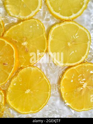 Gros plan citron dans liquide avec bulles. Tranches de citron mûr jaune dans l'eau. Gros plan sur des tranches de citron fraîches sur fond blanc Banque D'Images