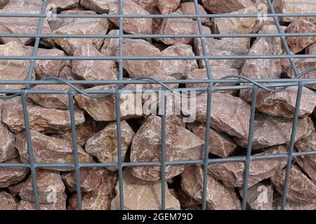 Pierres rouges dans le mur de Gabion en treillis soudé de fil, paniers, clôture de fil remplie de pierres de fond Banque D'Images