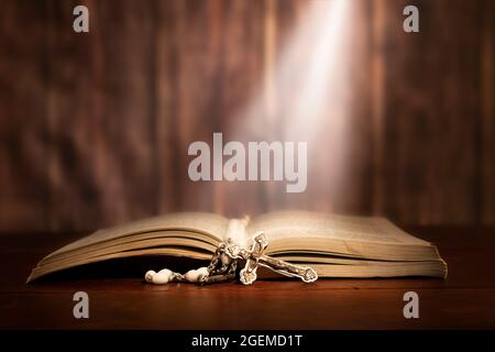 Image dramatique montrant un faisceau lumineux brillant brillant brillant sur une vieille bible avec un rosaire en face de lui. Banque D'Images