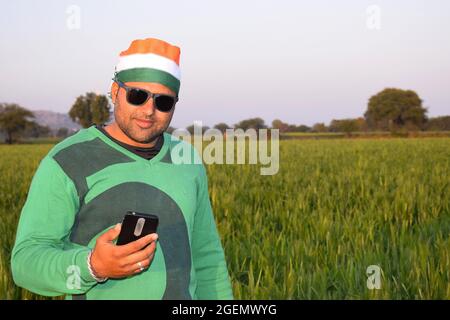 Portant un turban tricolore, un agriculteur indien parle sur son mobile le soir dans ses champs de blé, avec des lunettes Banque D'Images