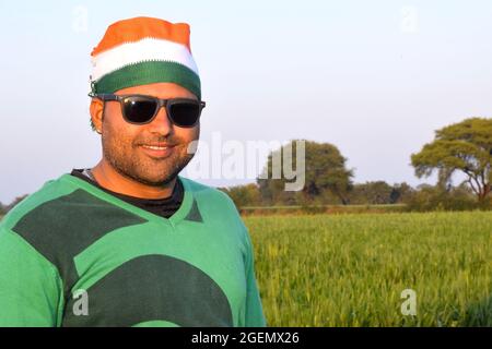 Portant un turban tricolore, un agriculteur indien parle sur son mobile le soir dans ses champs de blé, avec des lunettes Banque D'Images