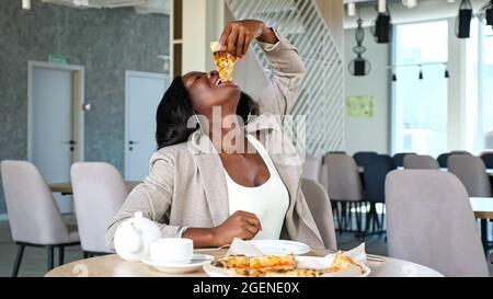 La femme afro-américaine apprécie une délicieuse pizza au café Banque D'Images
