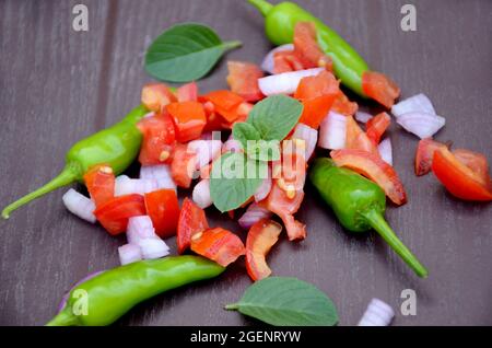 gros plan sur la tomate rouge tranchée avec des feuilles d'oignon, de chilly vert et de menthe sur un fond brun non focaré. Banque D'Images