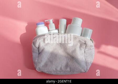 Par-dessus des bouteilles blanches assorties de produits de soin de la peau placées dans un sac cosmétique sur fond rose éclairé par la lumière du soleil Banque D'Images