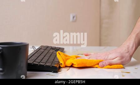 La main de l'homme nettoie le café renversé de la table et du clavier Banque D'Images