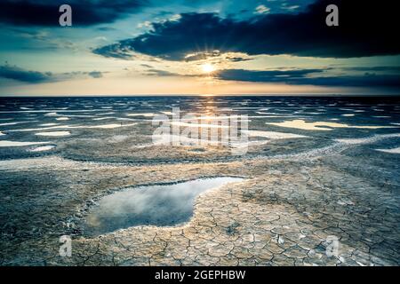 Bel été. La côte de la mer est inclinée par la pierre, le lever du soleil se reflète sur le sable humide. Paysage du matin. Banque D'Images