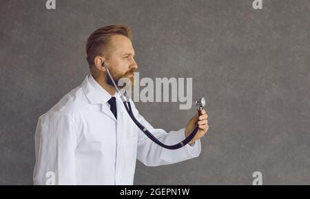 Un médecin caucasien adulte en manteau blanc à l'écoute du stéthoscope en studio Banque D'Images